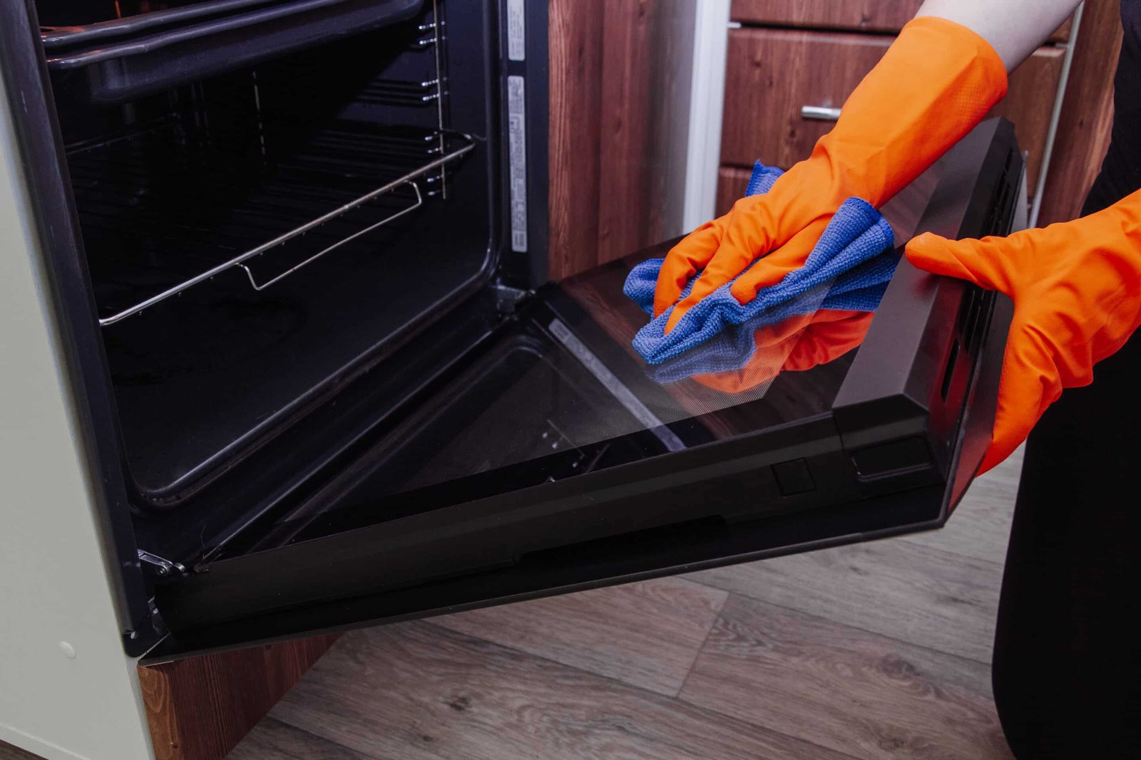 Women's hands in gloves with a microfiber cleaning cloth clean the oven door from the inside. Cleaning the oven